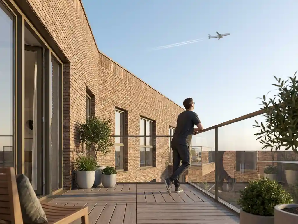 Person op modern Amsterdam balkon kijkt omhoog naar vliegtuig in blauwe lucht, warme bakstenen gevel op achtergrond