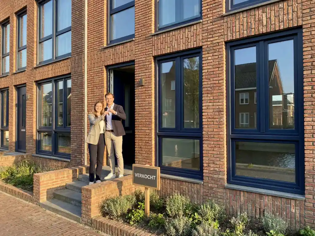 Jong stel met huissleutels voor verkocht Amsterdam grachtenpand met bakstenen gevel en grote ramen