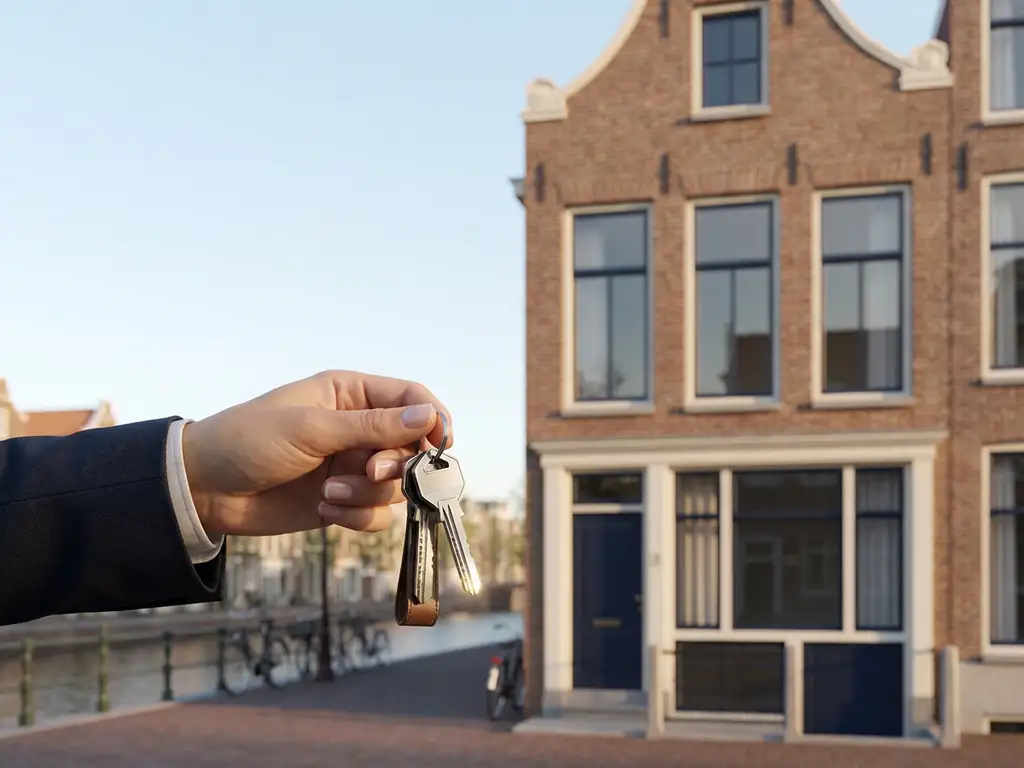 Makelaar reikt moderne huissleutels aan met Amsterdam grachtenpand op achtergrond